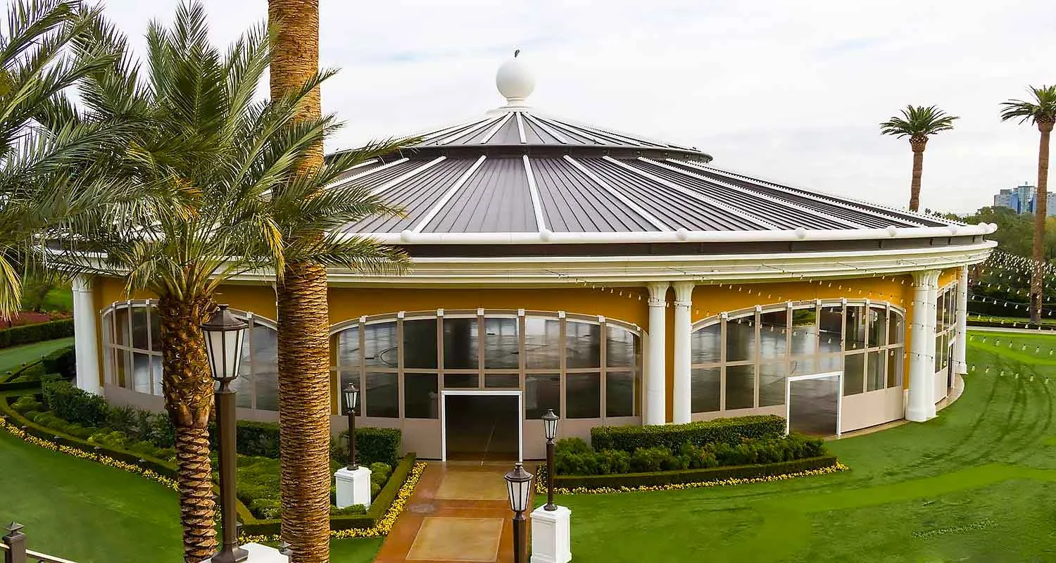 | Las Vegas Awning and StructuresA circular building with a dark metal roof and large windows is surrounded by palm trees and manicured lawns. The structure exemplifies Las Vegas shade systems, providing a blend of aesthetics and sun protection in a desert climate.