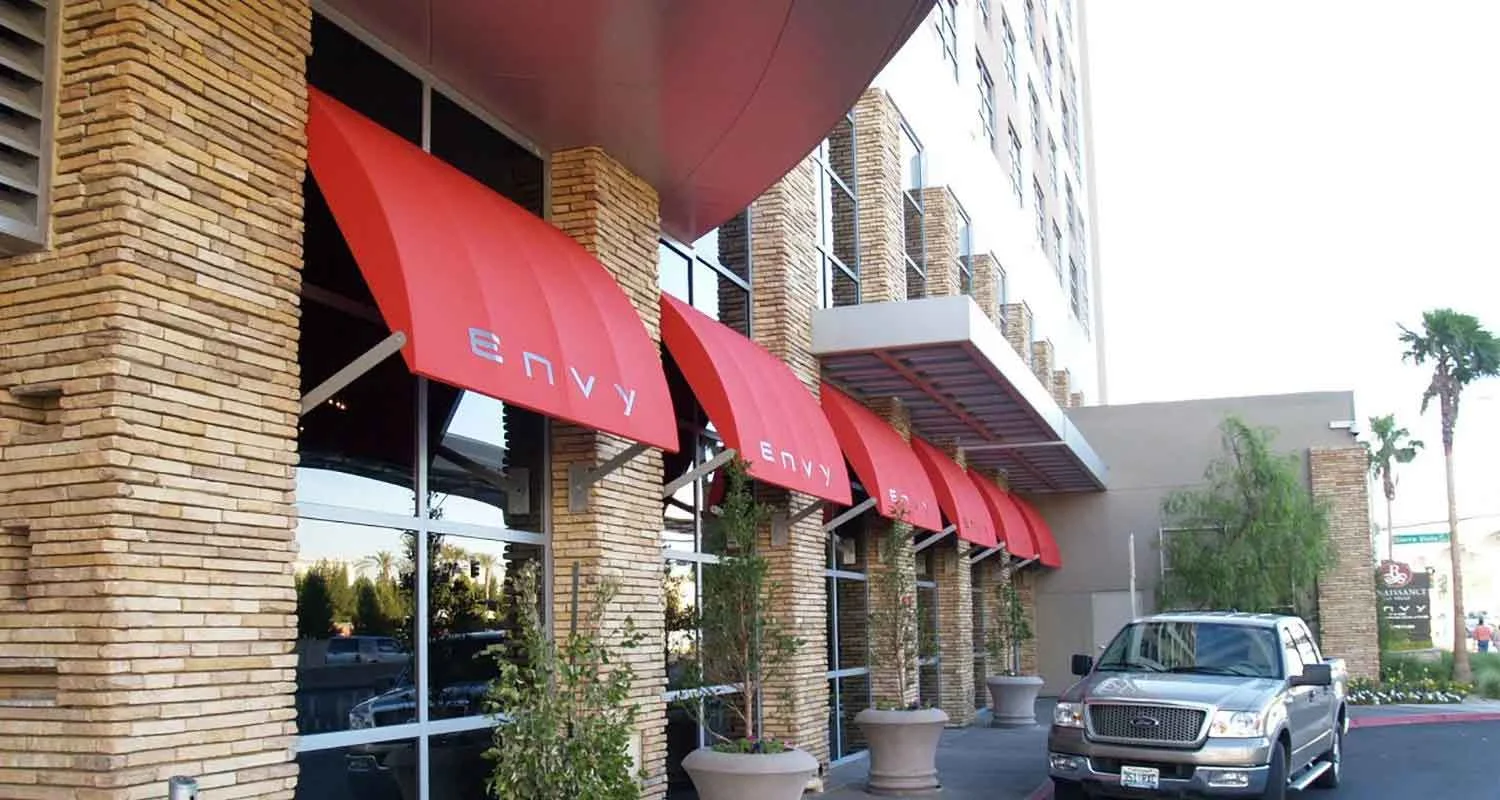 | Las Vegas Awning and StructuresThe image shows a row of red storefront awnings on a brick building, providing sun protection. A silver truck is parked nearby, highlighting Las Vegas awnings designed for desert shade solutions.